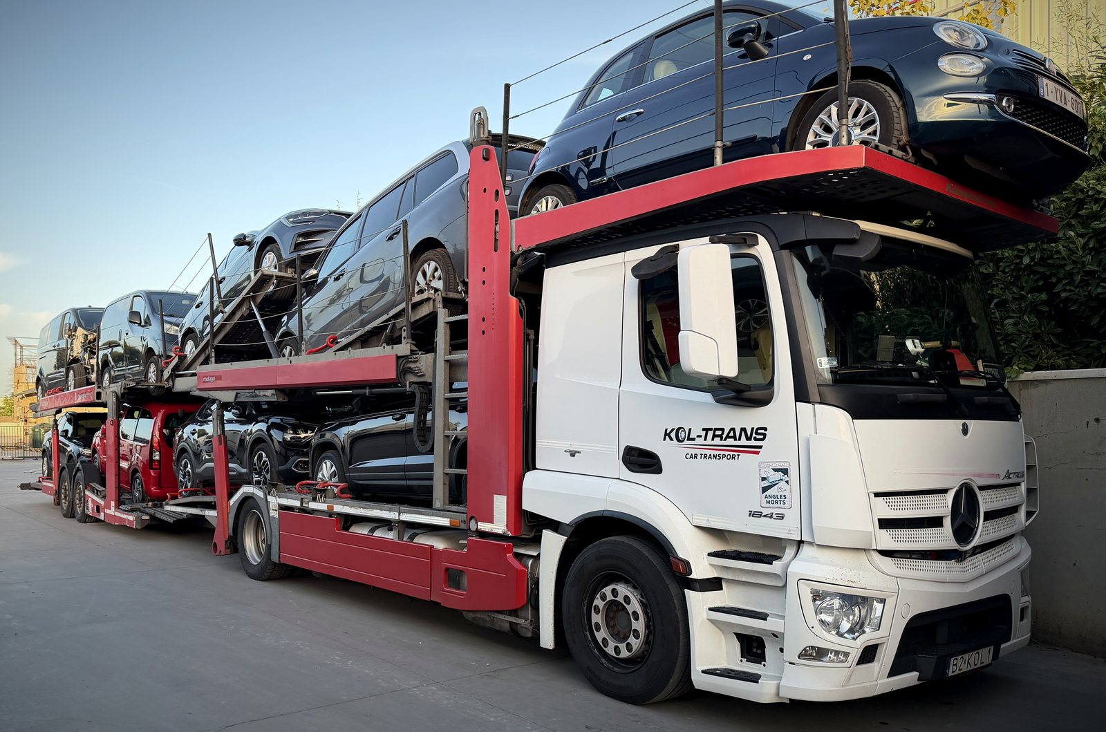 Biały Mercedes-Benz Actros Kol-Trans z czerwoną naczepą pełną samochodów, w dzień na placu w Belgii