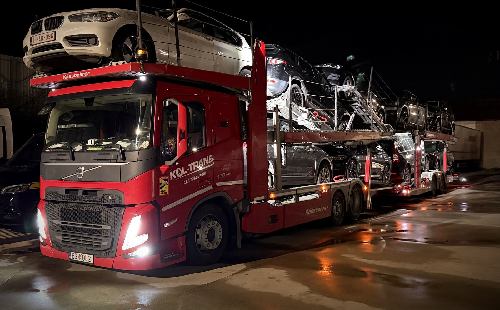 Czerwony autotransporter Volvo Kol-Trans z naczepą Kässbohrer załadowaną samochodami, nocą na placu w Belgii