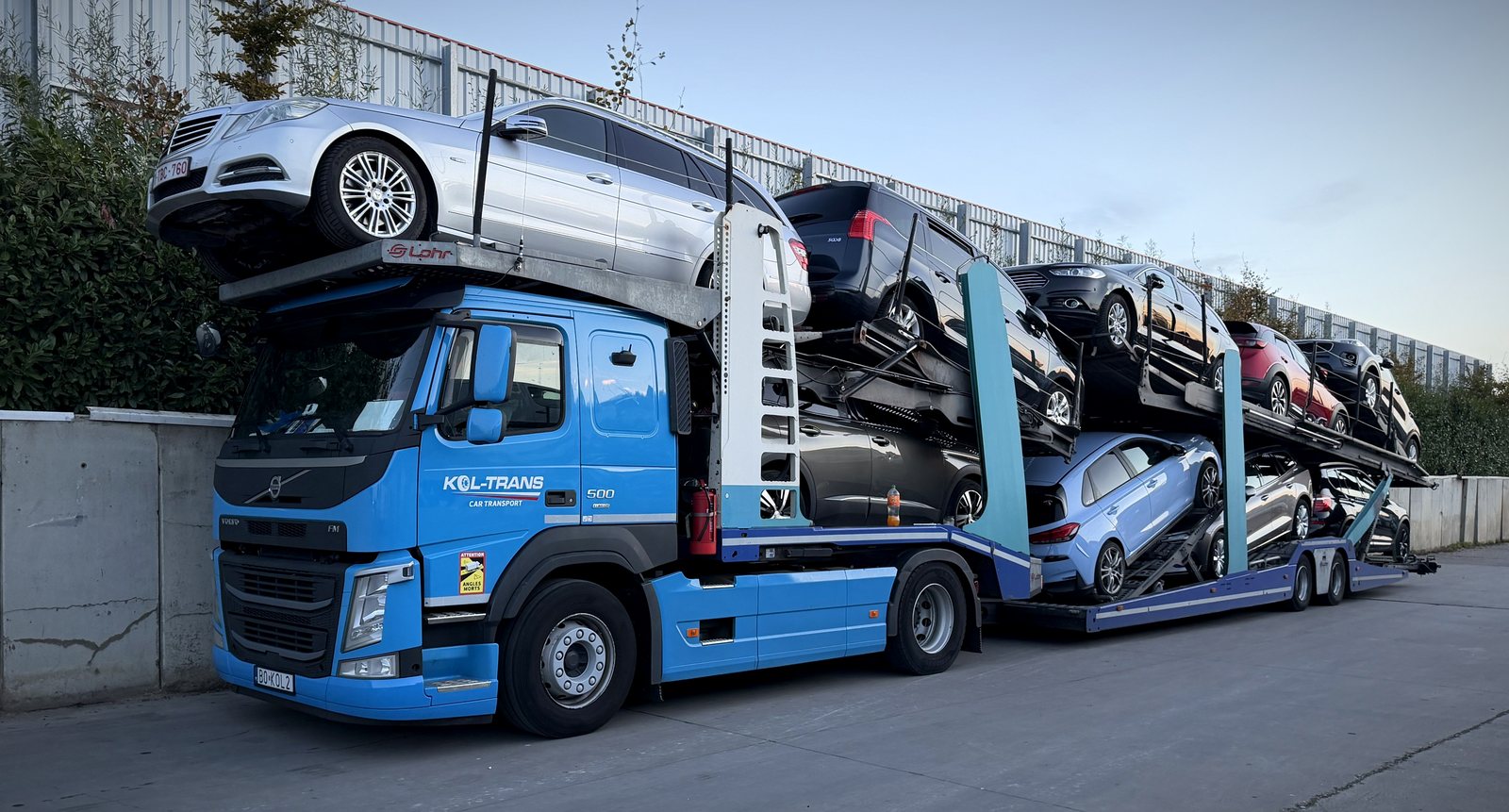 Niebieskie Volvo FM Kol-Trans z naczepą załadowaną samochodami, w dzień