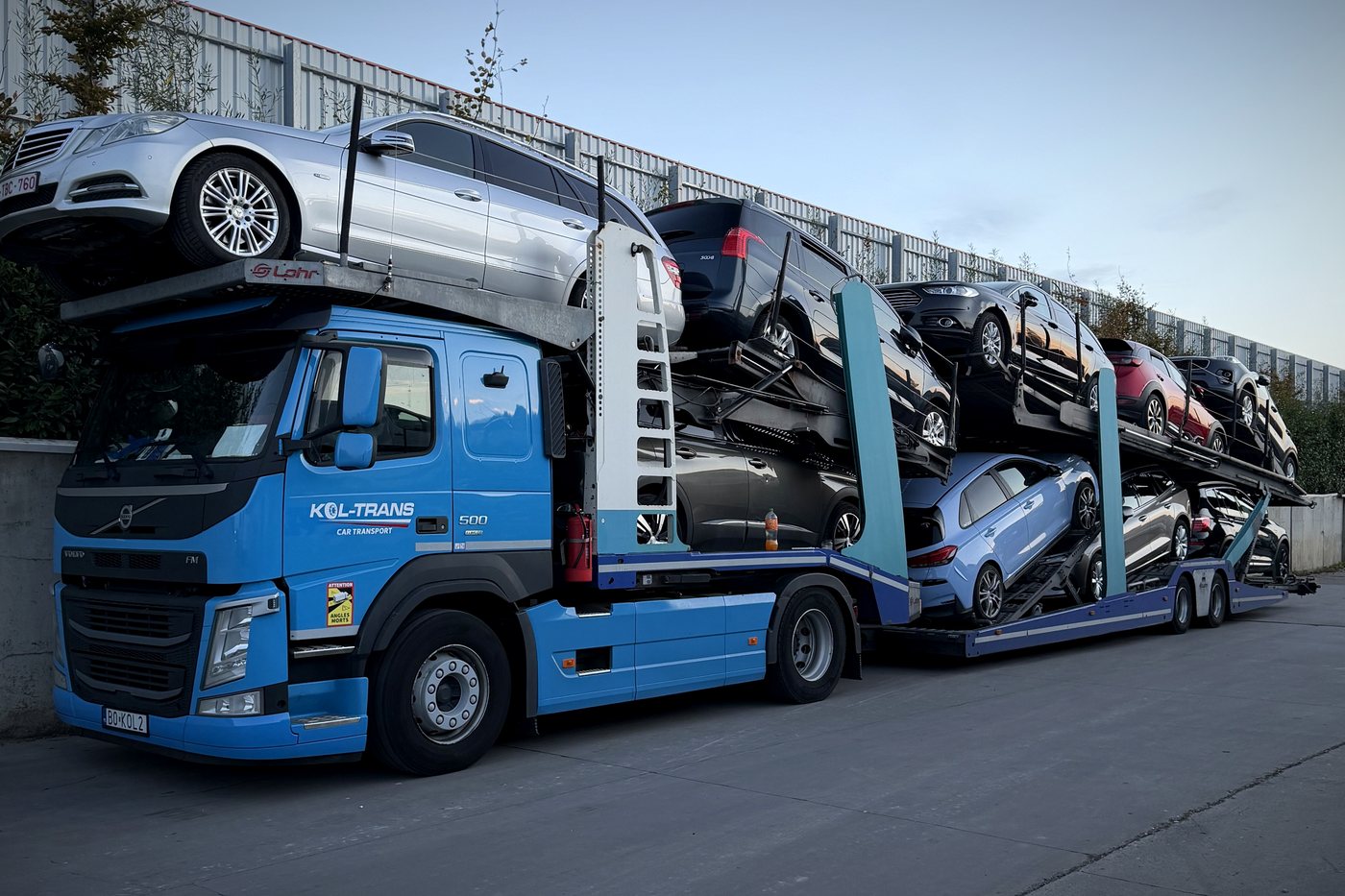 Cały załadowany zestaw Kol-Trans: niebieskie Volvo FM z naczepą Lohr pełną samochodów na placu w Belgii
